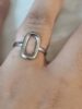 Bague argentée avec forme ovale sur un doigt.