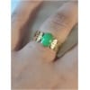 Bague en or avec pierre verte sur doigt.