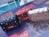 Trois sacs à main cloutés sur une table colorée.